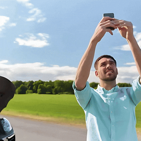 A Man In A Blue Shirt Is Taking A Picture Of A Field With His Phone GIF