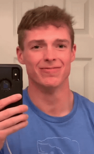 A Man In A Blue Shirt Is Taking A Selfie In Front Of A Mirror GIF