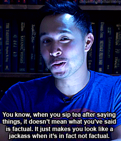 A Man In A Blue Shirt Is Talking In Front Of A Shelf Of Books GIF
