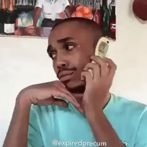 a man in a blue shirt is talking on a cell phone with a picture of a woman on the wall behind him .