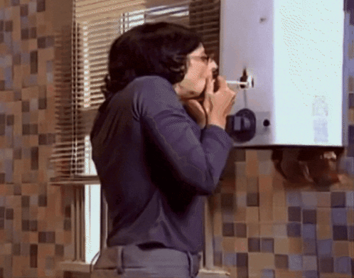 A Man In A Blue Shirt Is Talking On A Phone In Front Of A Wall With A Number 11 On It GIF