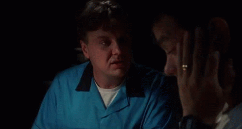 A Man In A Blue Shirt Is Talking To Another Man In A Dark Room . GIF