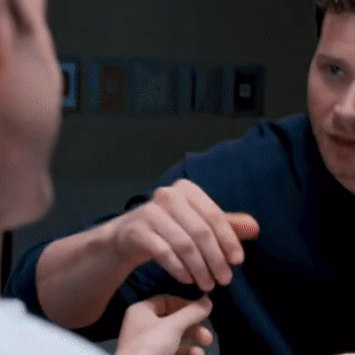 a man in a blue shirt is talking to another man in a dark room
