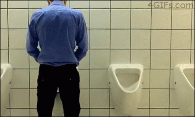 A Man In A Blue Shirt Is Urinating In A Bathroom GIF