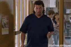 A Man In A Blue Shirt Is Walking Out Of A Doorway . GIF