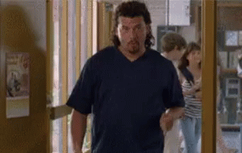 A Man In A Blue Shirt Is Walking Through A Doorway . GIF