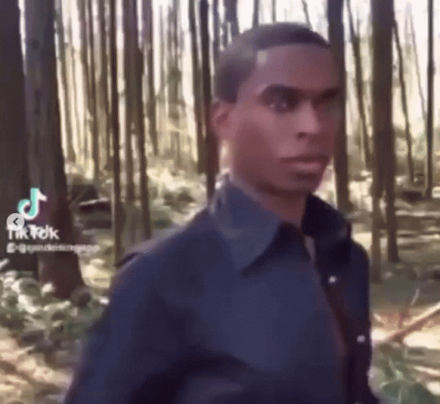 A Man In A Blue Shirt Is Walking Through A Forest . GIF