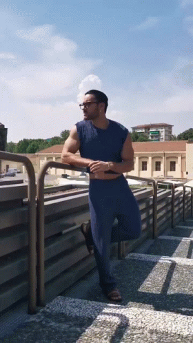 Man In Blue Shirt Leaning On Balcony Railing GIF