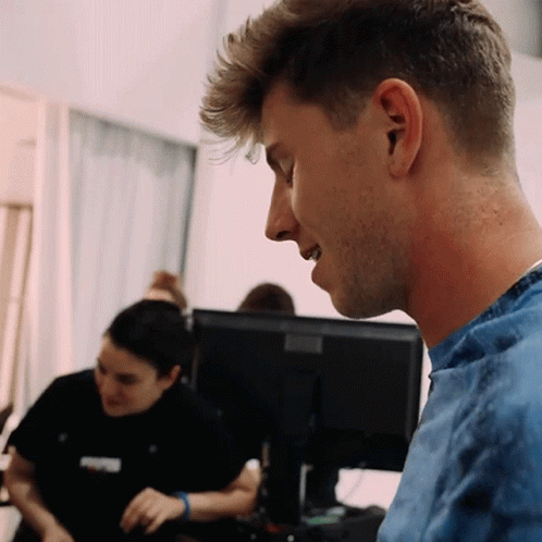 A Man In A Blue Shirt Looks At A Computer Screen GIF