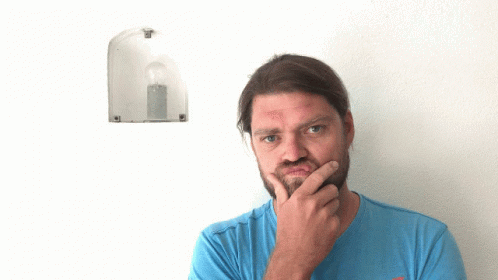 A Man In A Blue Shirt Points Up At A Light Bulb On A Wall GIF