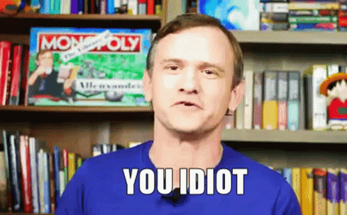 A Man In A Blue Shirt Says You Idiot In Front Of A Bookshelf GIF
