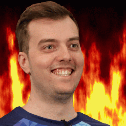 A Man In A Blue Shirt Smiles In Front Of A Fire Background GIF