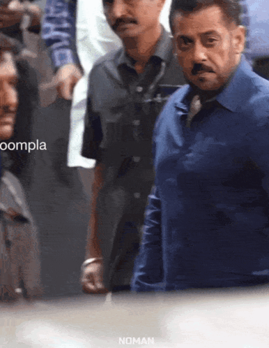A Man In A Blue Shirt Stands In A Crowd With The Word Noman On The Bottom GIF