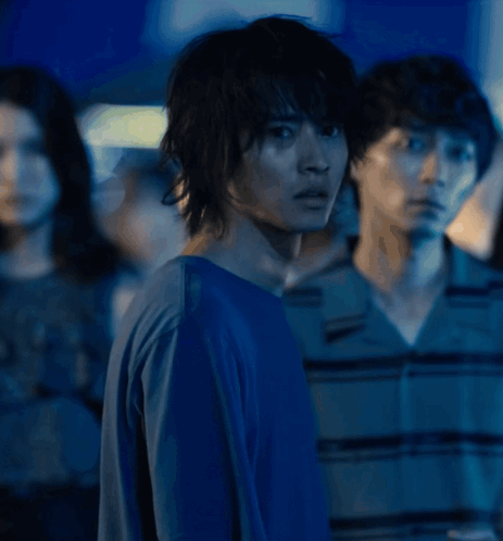 A Man In A Blue Shirt Stands In Front Of A Group Of People GIF