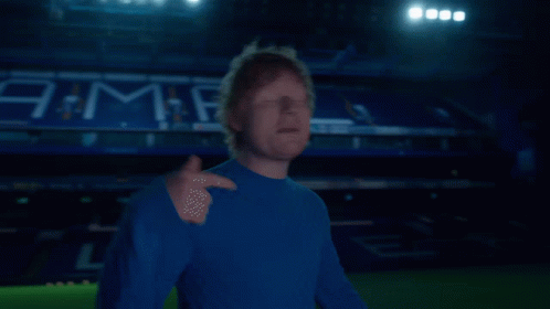 A Man In A Blue Shirt Stands In Front Of A Stadium That Has The Word Jama On It GIF