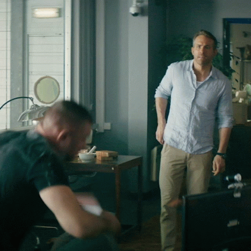 A Man In A Blue Shirt Stands Next To Another Man In Khaki Pants GIF