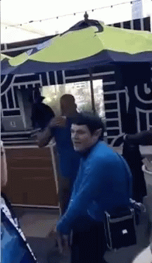 A Man In A Blue Shirt Stands Under An Umbrella GIF