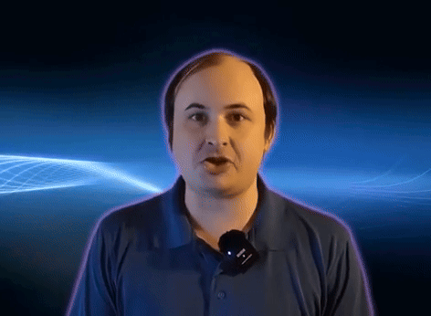 A Man In A Blue Shirt With A Microphone Around His Neck GIF
