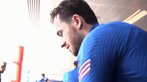 A Man In A Blue Shirt With A Red White And Blue Stripe On The Sleeve Looks Down GIF