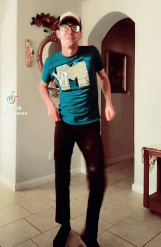 A Man In A Blue Shirt With The Letter M On It Is Dancing In A Hallway GIF