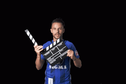 A Man In A Blue Sigma Shirt Is Holding A Clapper Board GIF