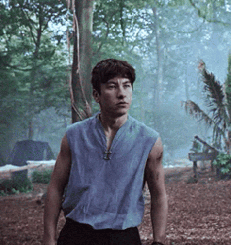 A Man In A Blue Sleeveless Shirt Is Standing In The Woods GIF