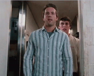 A Man In A Blue Striped Shirt Stands In A Hallway GIF