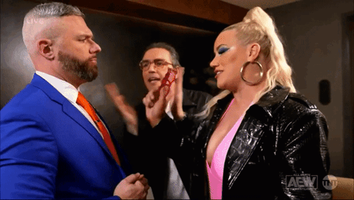 A Man In A Blue Suit And A Woman In A Pink Top Are Standing Next To Each Other In A Room . GIF