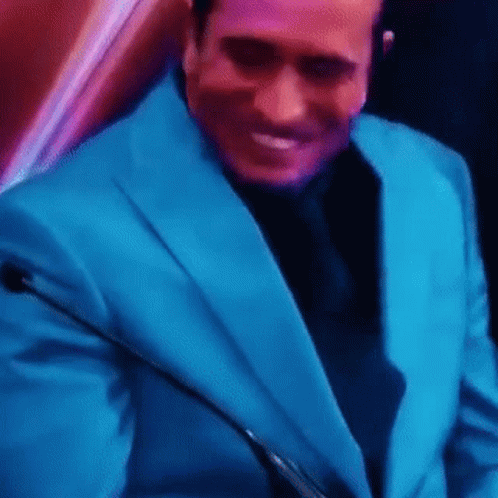 A Man In A Blue Suit And Black Tie Is Smiling While Holding A Microphone . GIF