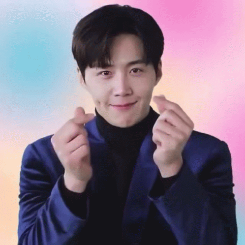 A Man In A Blue Suit And Black Turtleneck Is Making A Heart Shape With His Hands GIF
