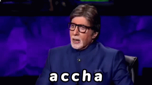 A Man In A Blue Suit And Glasses Is Sitting In Front Of A Purple Background And Making A Funny Face . GIF