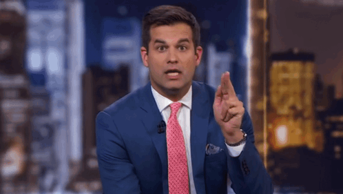 a man in a blue suit and pink tie is pointing his finger
