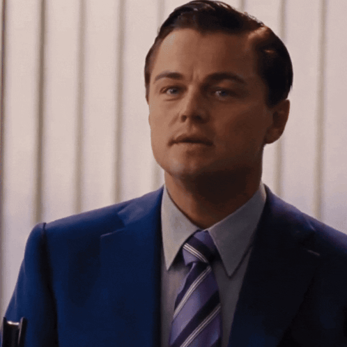 A Man In A Blue Suit And Purple Tie Looks At The Camera GIF