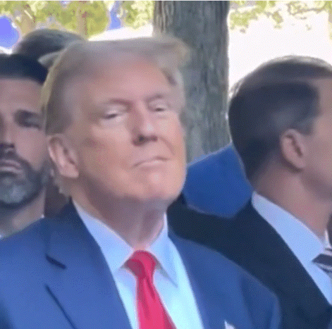 A Man In A Blue Suit And Red Tie Is Sitting In A Crowd Of People . GIF