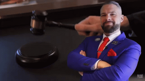 A Man In A Blue Suit And Red Tie Stands In Front Of A Judge 'S Gavel With The Number 113 On It GIF