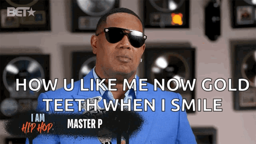 A Man In A Blue Suit And Sunglasses Says How U Like Me Now Gold Teeth When I Smile GIF