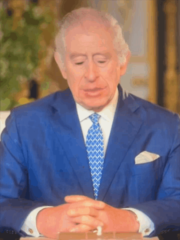A Man In A Blue Suit And Tie Is Sitting At A Table With His Eyes Closed GIF