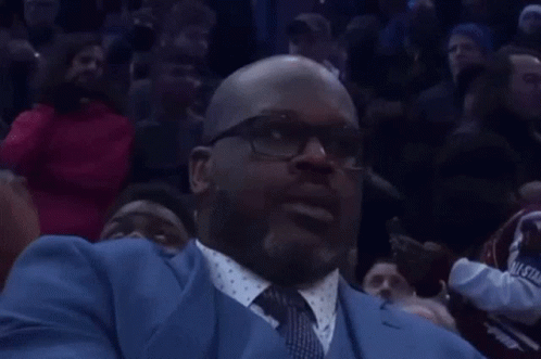 a man in a blue suit and tie is sitting in a crowd watching a basketball game