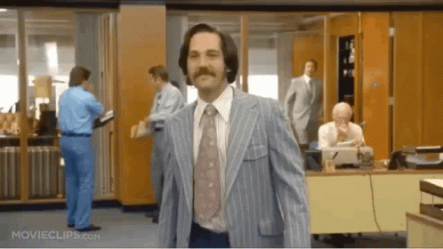 A Man In A Blue Suit And Tie Is Walking Through An Office . GIF
