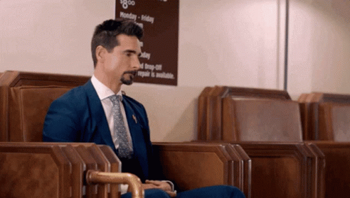 A Man In A Blue Suit And Tie Sits In Front Of A Sign That Says Monday - Friday GIF