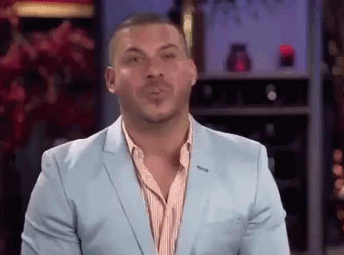 A Man In A Blue Suit Is Blowing A Kiss While Standing In Front Of A Wine Rack . GIF