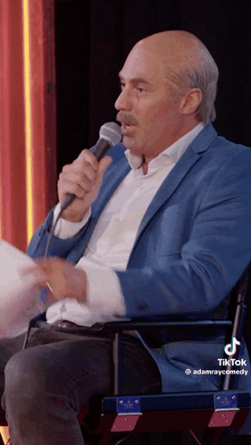 A Man In A Blue Suit Is Holding A Microphone In His Hand GIF