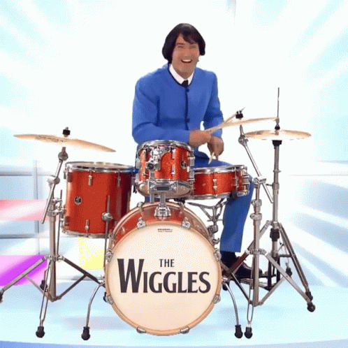 A Man In A Blue Suit Is Playing A Drum Set That Says The Wiggles On It GIF