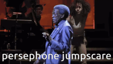 A Man In A Blue Suit Is Singing Into A Microphone With The Words Persephone Jumpscare Behind Him GIF