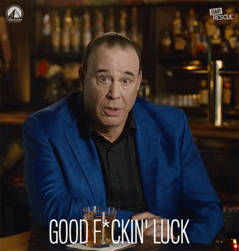 A Man In A Blue Suit Is Sitting At A Bar Holding A Glass Of Whiskey And Says Good F * Cking Luck GIF