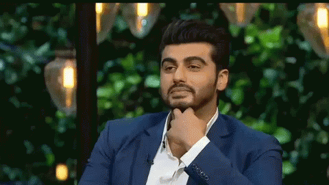 A Man In A Blue Suit Is Sitting In Front Of A Green Background With His Hand On His Chin . GIF