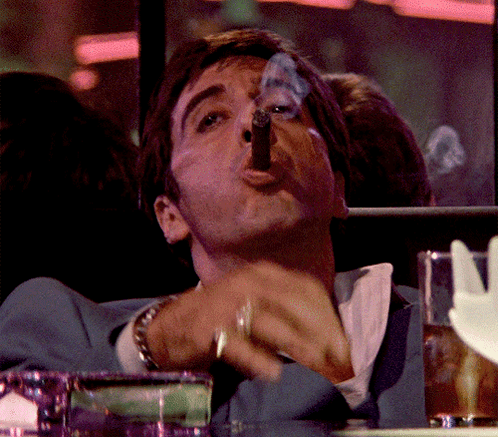 A Man In A Blue Suit Is Smoking A Cigar With Smoke Coming Out Of His Mouth GIF