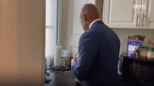 A Man In A Blue Suit Is Standing In A Kitchen With A Bag Of Purple Powder On The Counter .. GIF