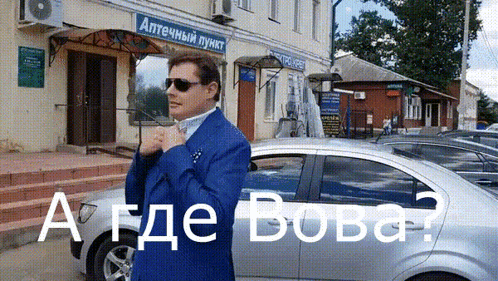 A Man In A Blue Suit Is Standing In Front Of A Building That Says " Аптечный Пункт " On It GIF