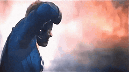A Man In A Blue Suit Is Standing In Front Of A Cloudy Sky . GIF